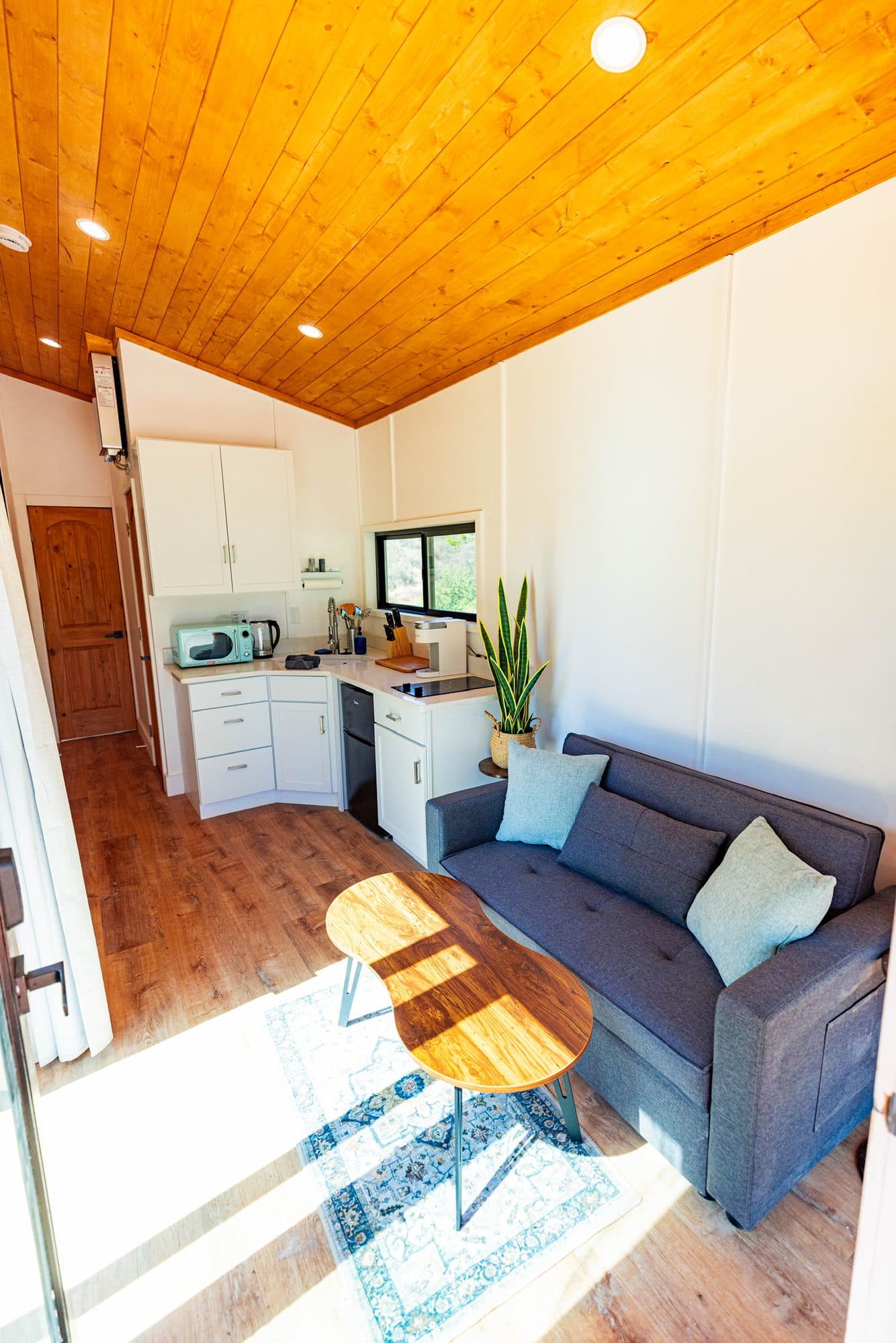 Living room with a blue sofa and a wood coffee table, the kitchen behind