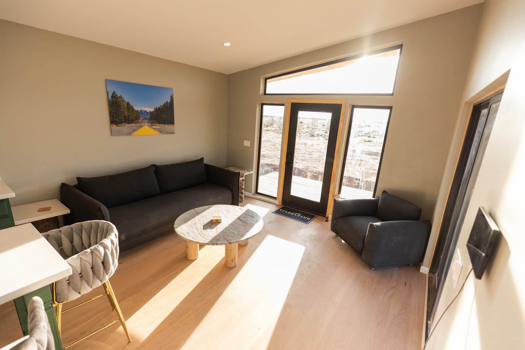 Living room with a dark sofa, an armchair and glass doors in afternoon sun