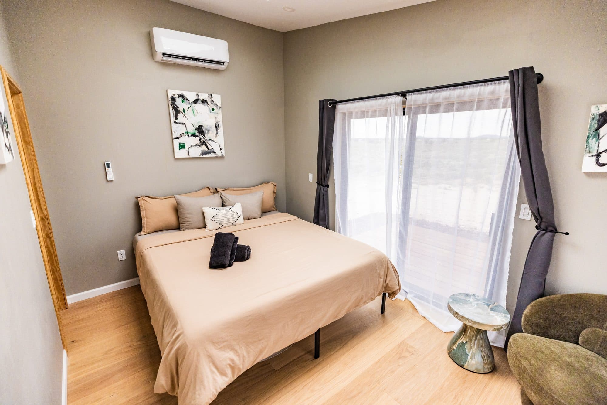 Bedroom with the bed, a mini split and sheer curtains over the sliding doors